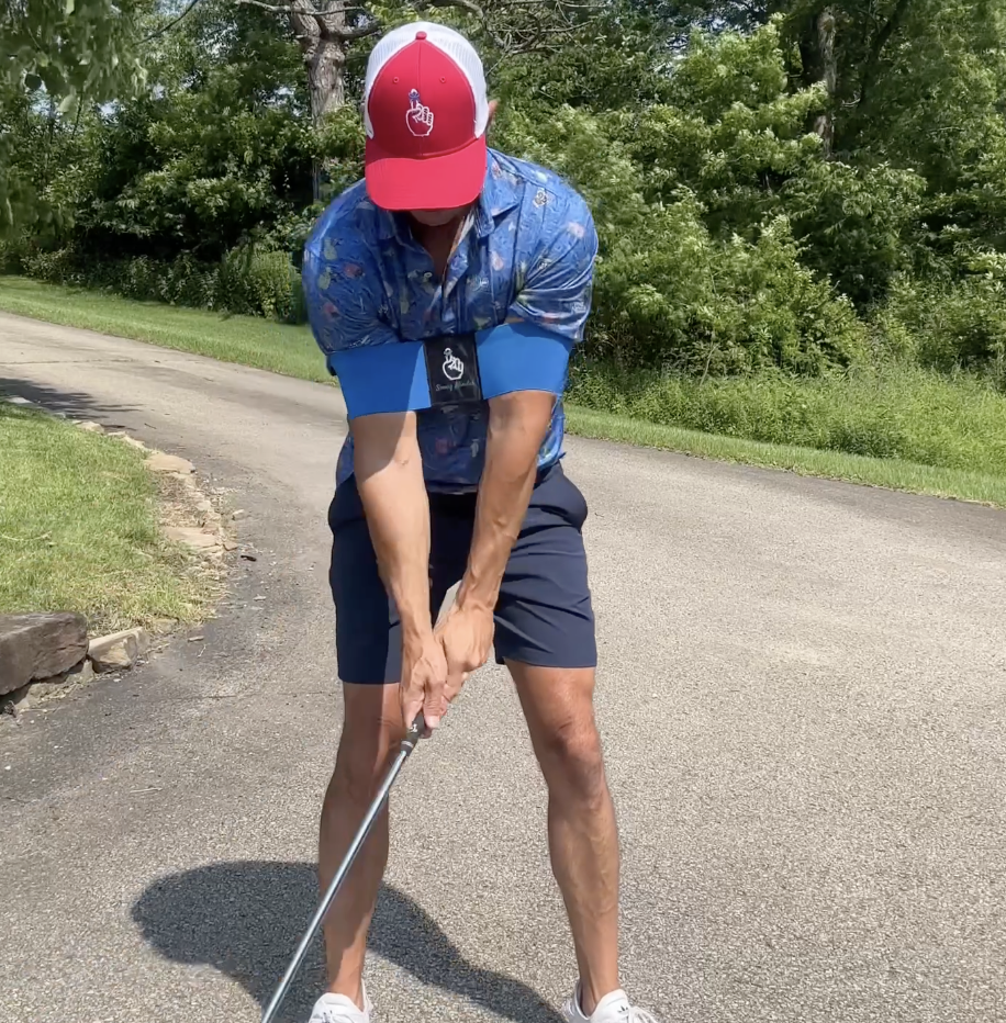Person playing golf on a paved path with greenery in the background