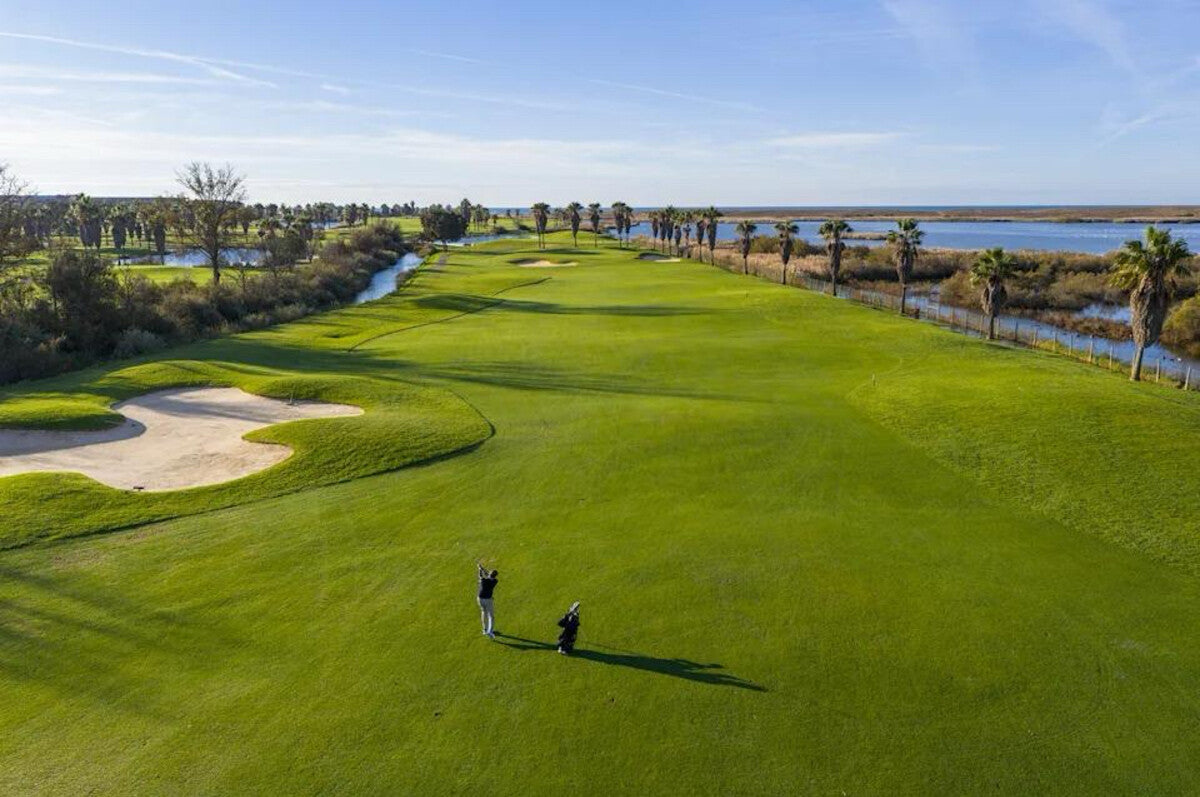 Golfer on a broad fairway with a bunker and water alongside the hole.